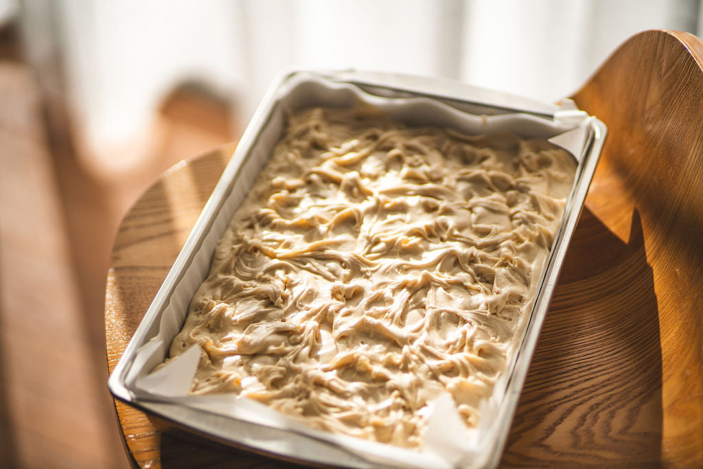 Tray of lemon meringue fudge with a swirled, creamy top sitting on a wooden chair in soft natural light.