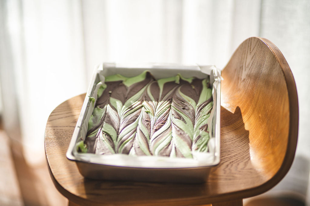 Tray of chocolate mint swirl fudge with green and dark chocolate marbled pattern, photographed on a wooden chair in soft natural light.