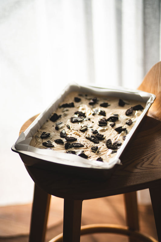 Tray of cookies and cream fudge topped with crushed chocolate biscuits, resting on a wooden chair in soft natural light.