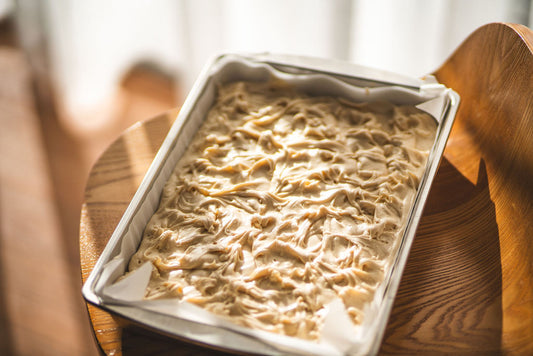 Tray of lemon meringue fudge with a swirled, creamy top sitting on a wooden chair in soft natural light.