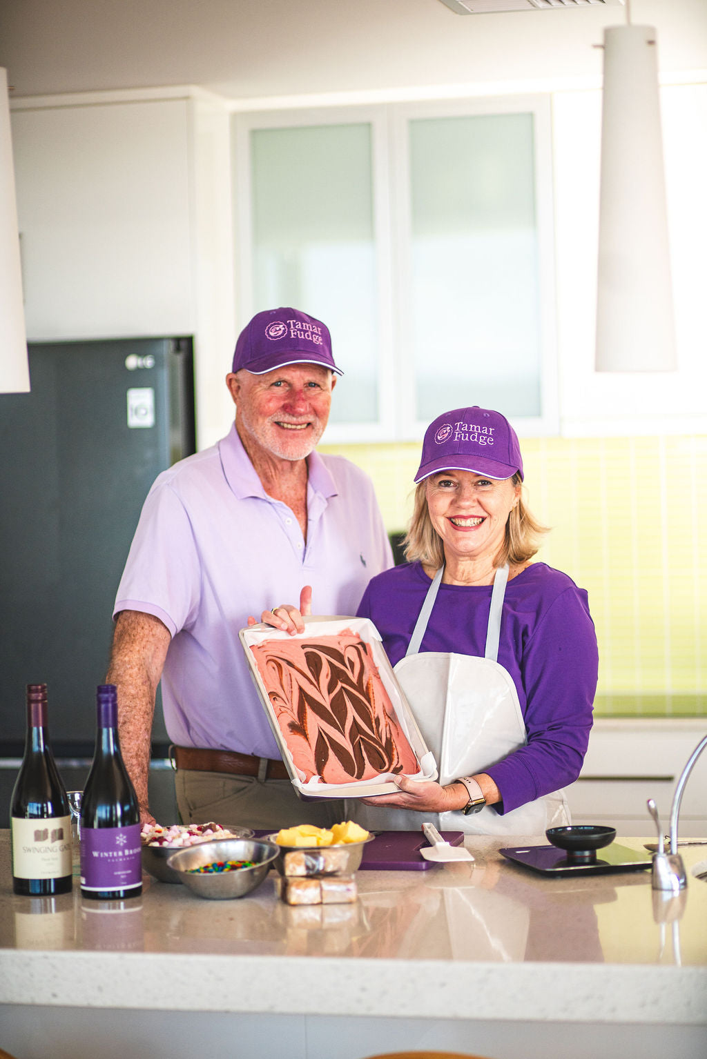Two Tamar Fudge makers smiling in a kitchen, holding a tray of swirled fudge.