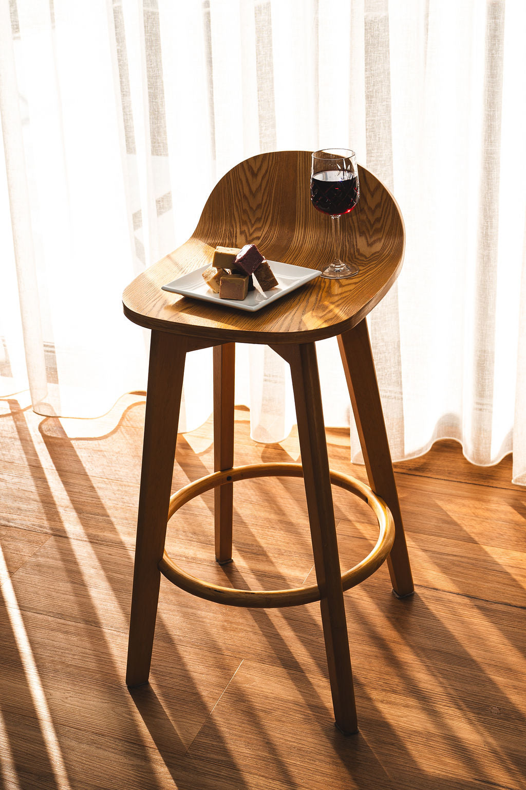 Plate of assorted fudge pieces and a glass of red wine on a wooden chair in warm natural light.