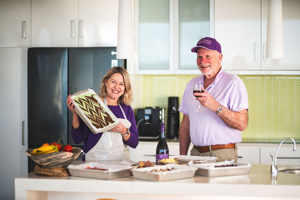 Two Tamar Fudge makers smiling in a kitchen, holding a tray of swirled fudge