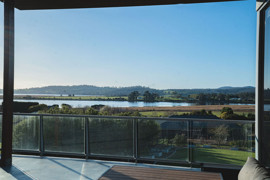 Scenic view of the Tamar Valley from a balcony overlooking the river, fields and distant hills under a clear blue sky.