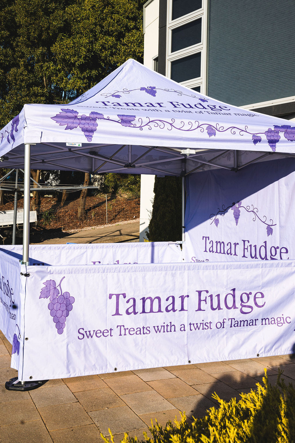Tamar Fudge branded canopy tent outdoors with trees and building in the background
