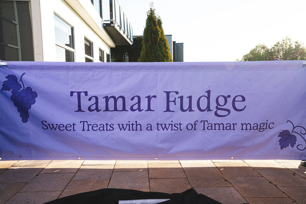 Outdoor banner reading ‘Tamar Fudge – Sweet Treats with a twist of Tamar magic’ with grape illustrations on each side.