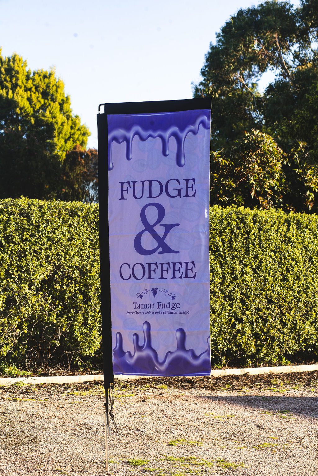 Outdoor banner reading ‘Fudge & Coffee – Tamar Fudge’ displayed in front of green hedges.